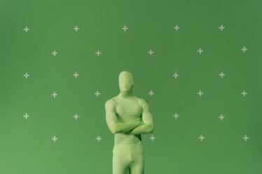 Pessoa com traje verde de chroma key, braços cruzados, diante de uma tela verde com marcadores de rastreamento