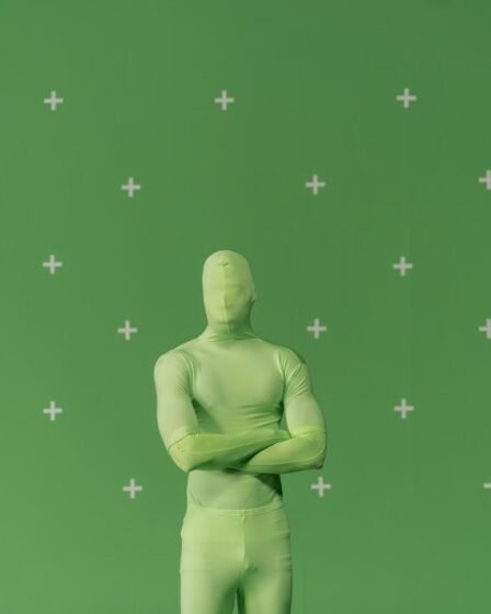 Pessoa com traje verde de chroma key, braços cruzados, diante de uma tela verde com marcadores de rastreamento