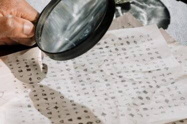 Mão segurando uma lupa sobre papéis com símbolos cifrados