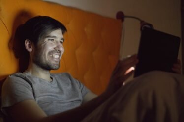 Homem sorrindo na cama à noite enquanto assiste a algo em um tablet