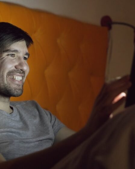 Homem sorrindo na cama à noite enquanto assiste a algo em um tablet