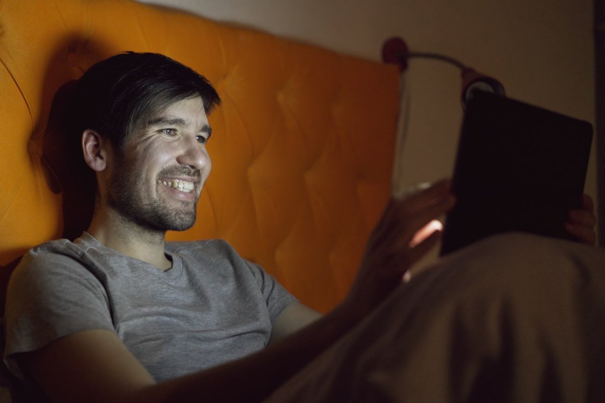 Homem sorrindo na cama à noite enquanto assiste a algo em um tablet