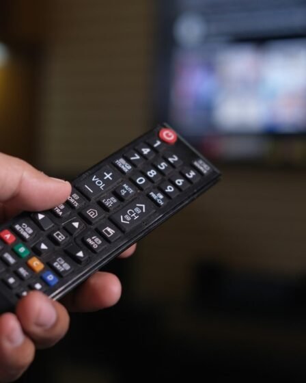Mão segurando um controle remoto diante de uma TV desfocada